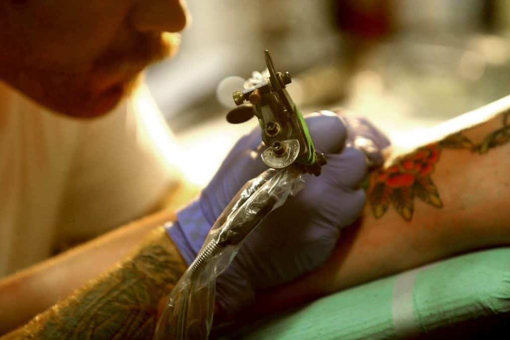 An artist is applying a tattoo to his clients arm. - Can You Workout After Getting a Tattoo