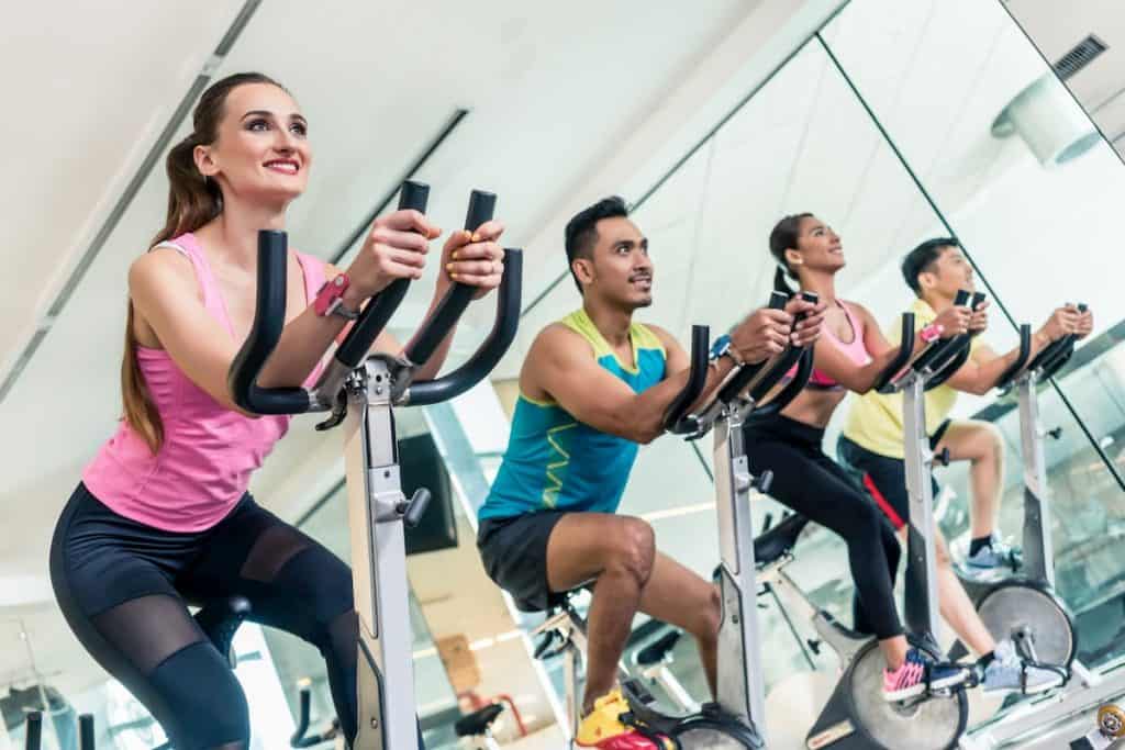 Side view of a beautiful fit young women smiling while pedaling during cardio workout at indoor cycling group class in a modern fitness club - How Many Times a Week Should I do HIIT