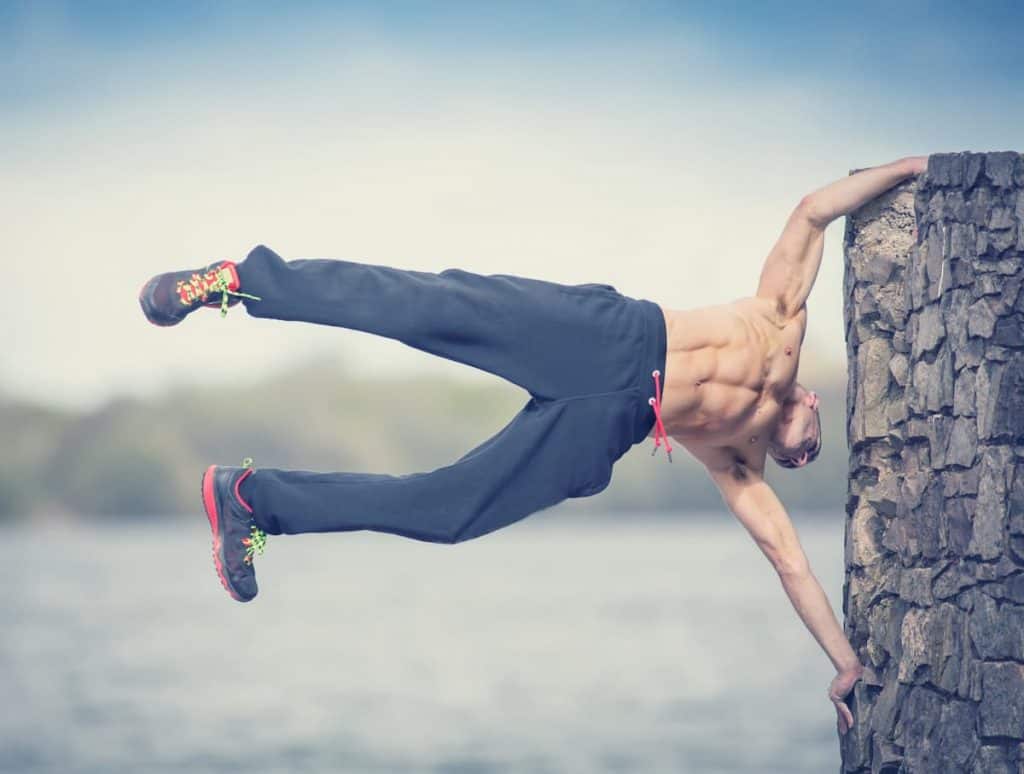 Urban fitness workout calisthenics, male in flag pose on wall over water - is calisthenics better than weightlifting