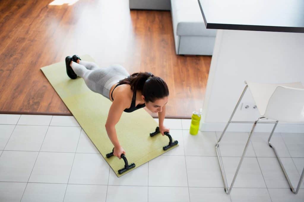 A Woman in plank position using push up stands - Should I Use Push Up Handles