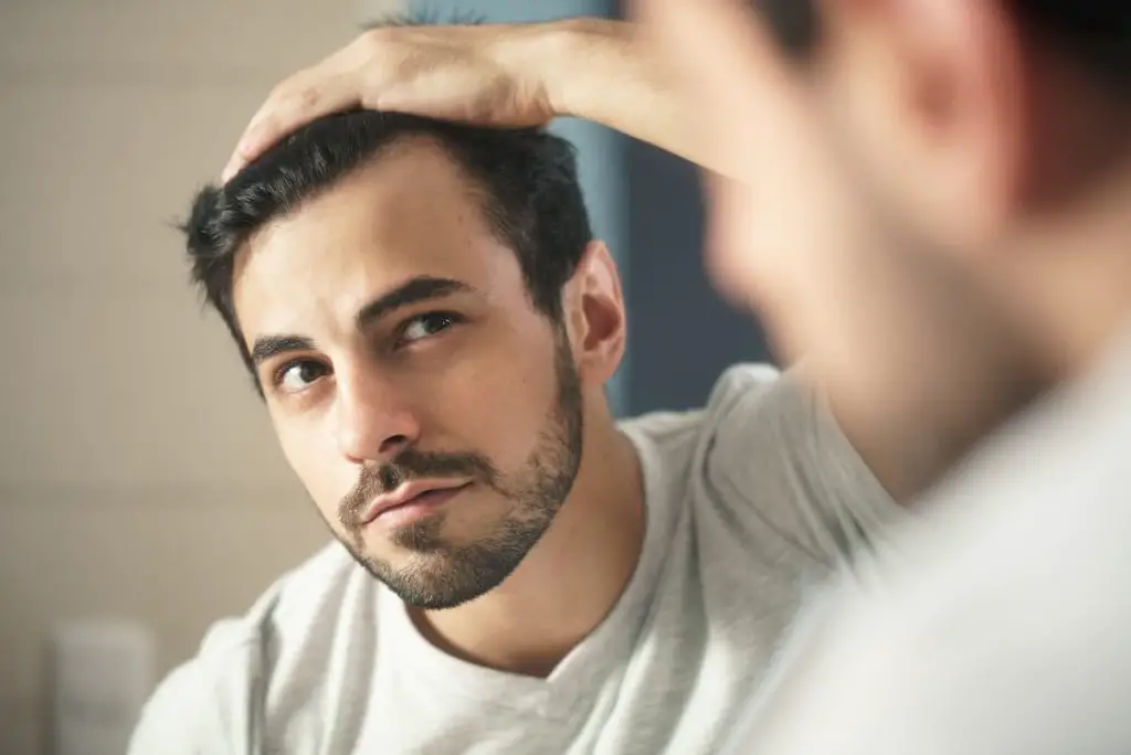 man worried for hair loss and looking at mirror his receding hairline - hair loss on keto diet