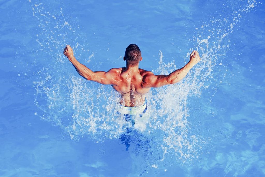 Young man pushing up out of the water - post on Can You Build Your Muscle Tone Through Swimming