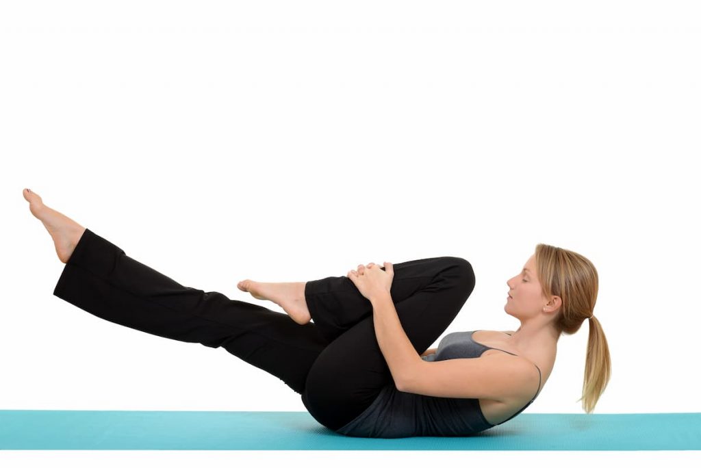 Woman doing Pilates single leg stretch one leg pulled to chest other leg lifted a foot off the ground and shoulders pulled up working the abs